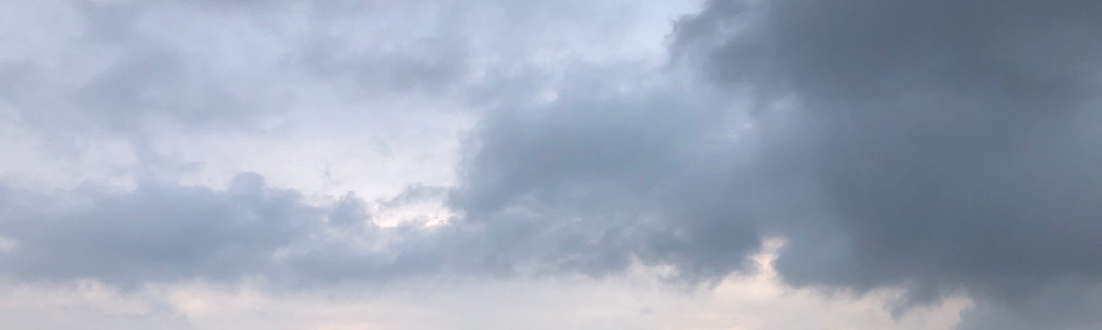 Clouds partly covering a predawn sky. Grass and trees are dark green in the early morning.