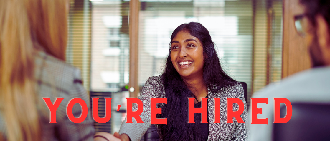 image of woman in a job interview. Text reads “you’re hired. “