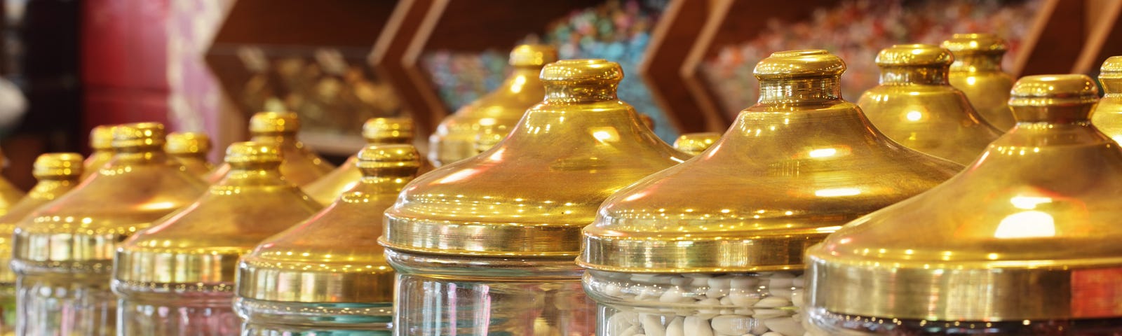 A row of large glass jars with brass lids, each filled with brightly coloured candy. More can be seen in the background.