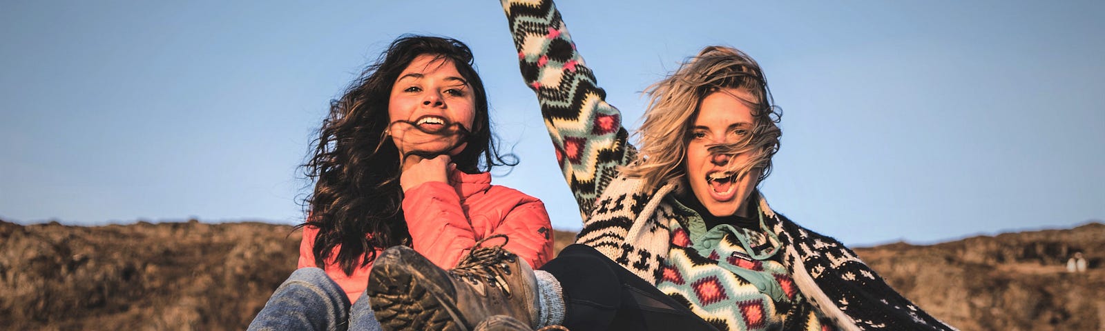 Two girls sitting on top of vehicle with wind blowing in their hair