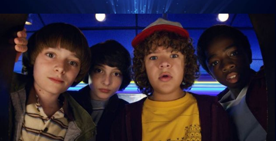 Four of the younger characters from Stranger Things looking down at the camera