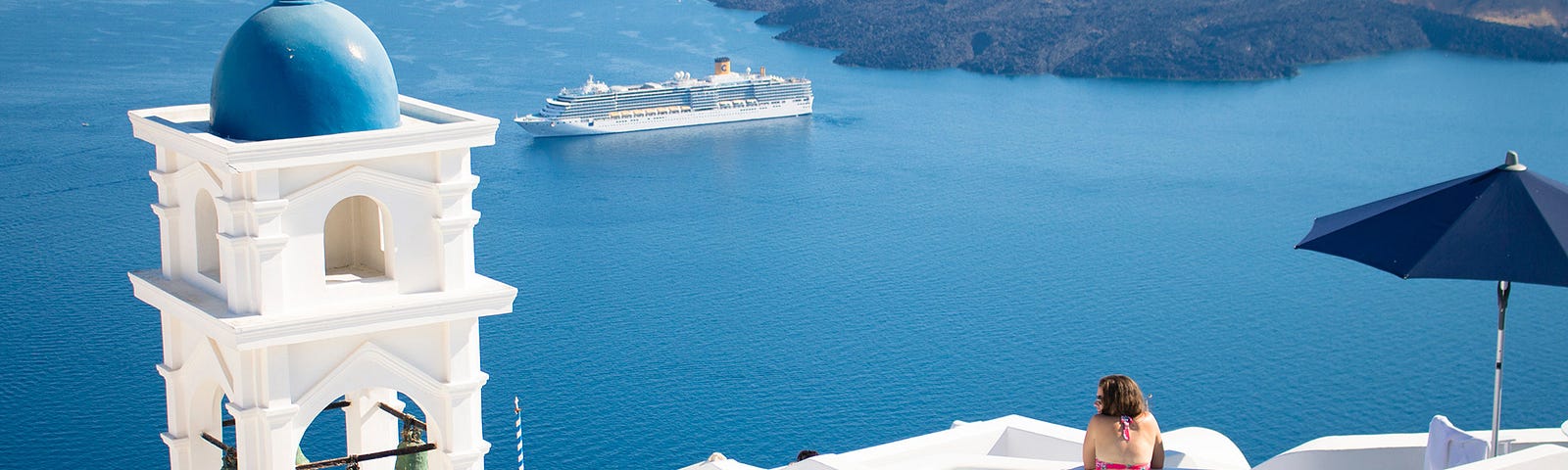 Woman in a rooftop pool in Santorini overlooking the water with cruise ship in the distance