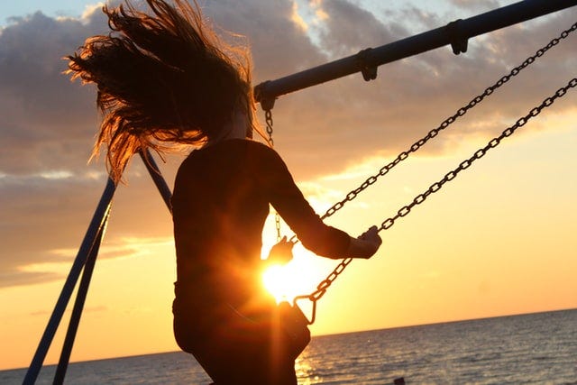 Image of a woman riding a swing at sunset