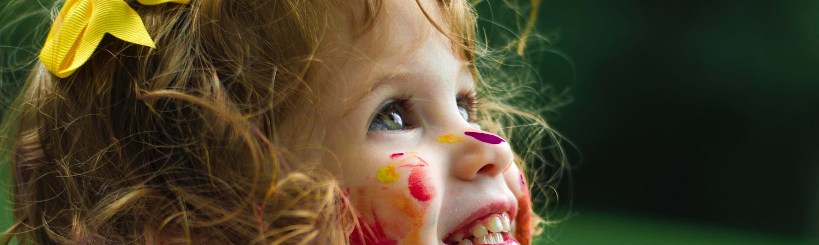 Smiling toddler, covered with paint, sitting outside on a blanket