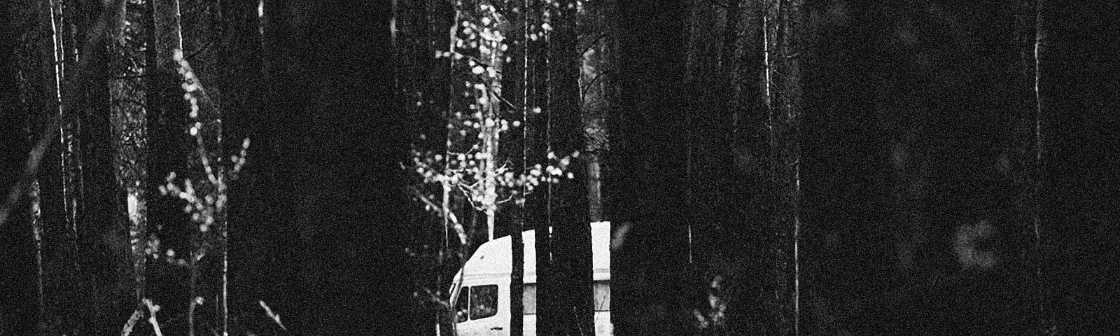 Black and white photo of van in woods.