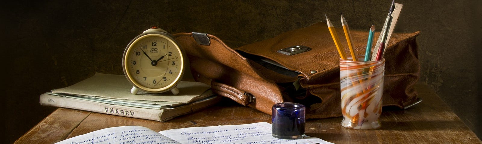 A notebook, bag, and pencil on a wooden desk.
