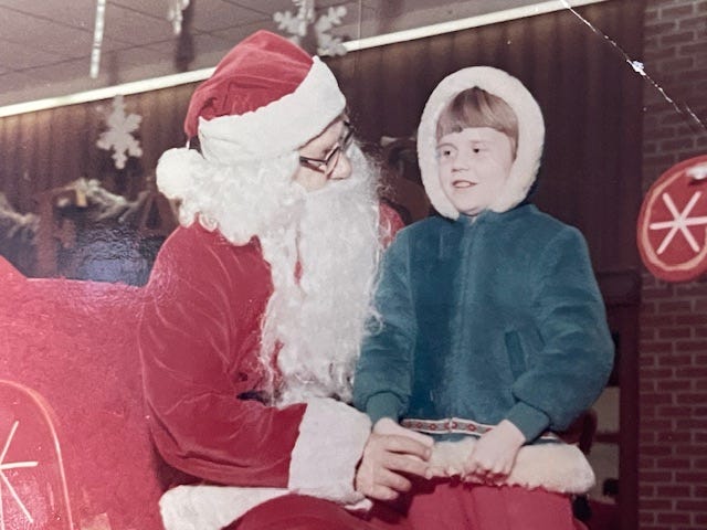 Santa with a little girl in a blue coat with her hood up.