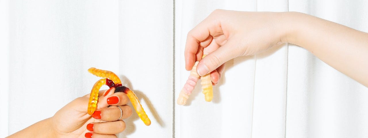 Two hands hold gummy worms over a white background.