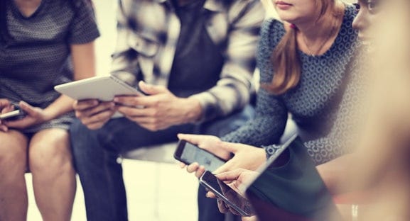 Teenagers sitting holding a cellphone and notebook.