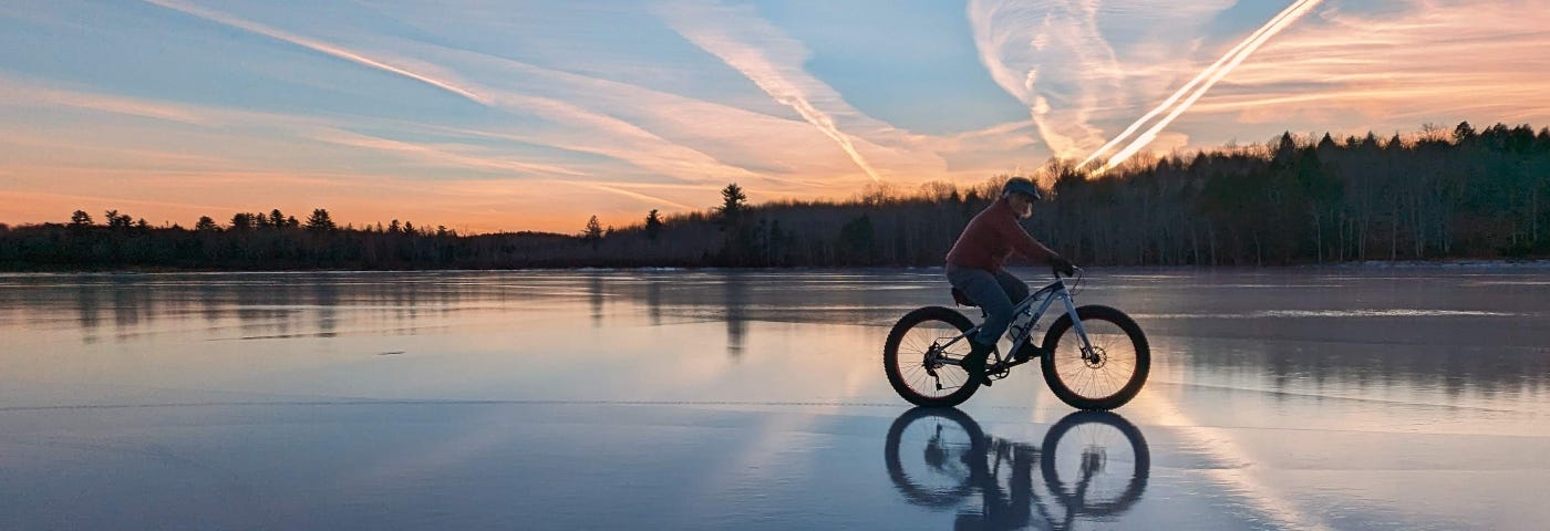 A woman rides a fat bike across a frozen pond.