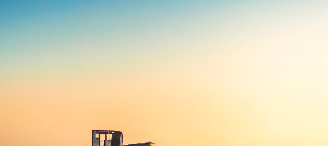 A solitary old wooden boat sits in calm water at sunrise