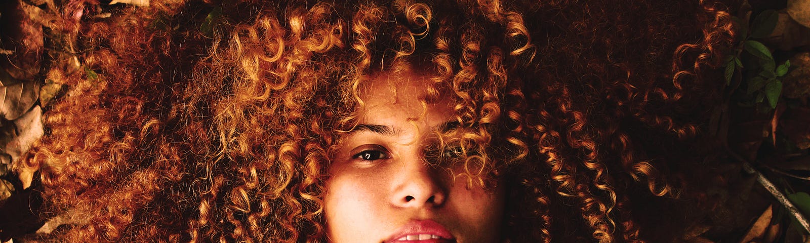 Woman with a curly afro lays on a pile of leaves