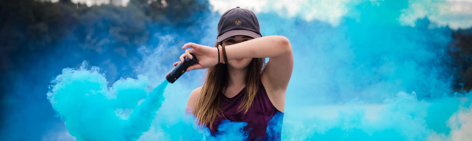 Woman in a baseball cap and a tank top waves a blue smoke flare.