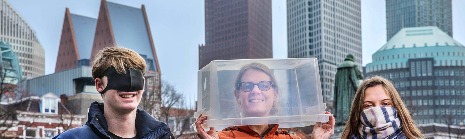 Jongen met een mondkapje over zijn ogen, vrouw met een doorzichtige doos op haar hoofd en meisje met een sjaal voor haar mond