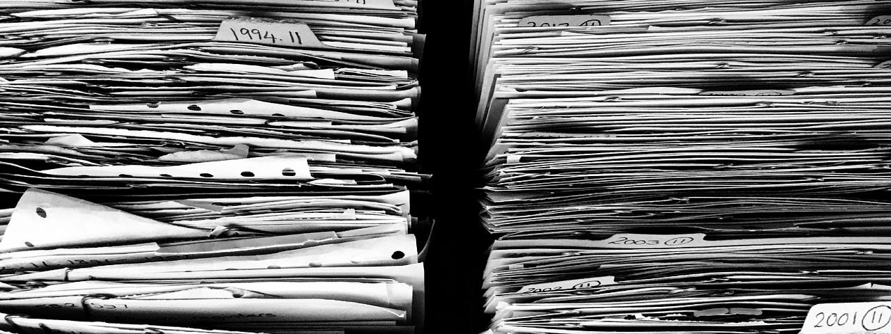 IMAGE: Two big stacks of paper files with a few labels, in black and white