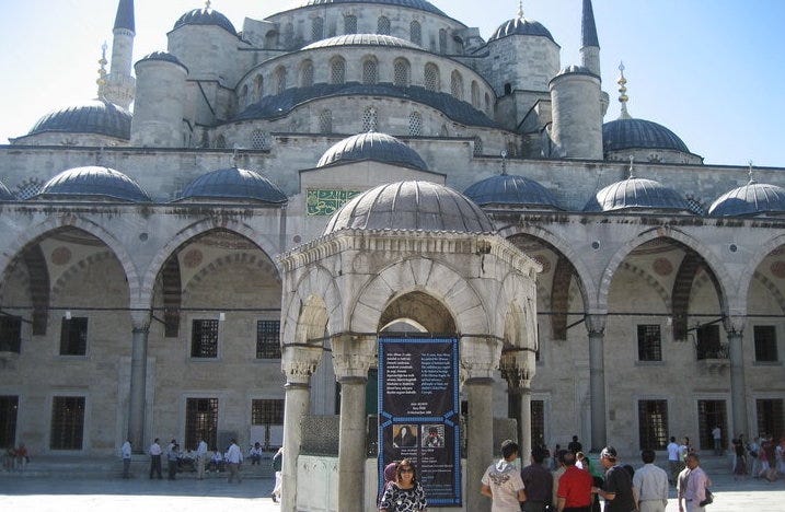 The Blue Mosque in Istanbul with a girl standing in front of it and the ticket counter to enter with many visitors waiting to buy their entrance ticket