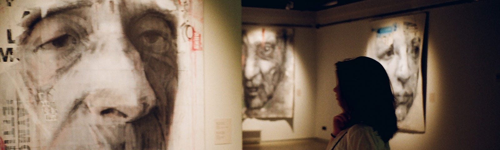 Woman standing in gallery looking at large portrait.