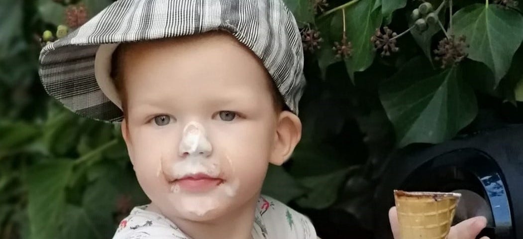 A young boy holding a cone with ice cream on his nose and chin.