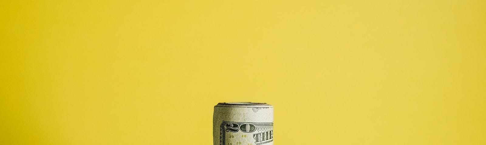 A roll of American money on a yellow background.