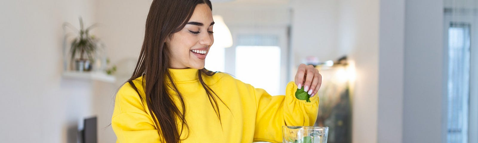 A woman in a yellow sweater making a smoothie.