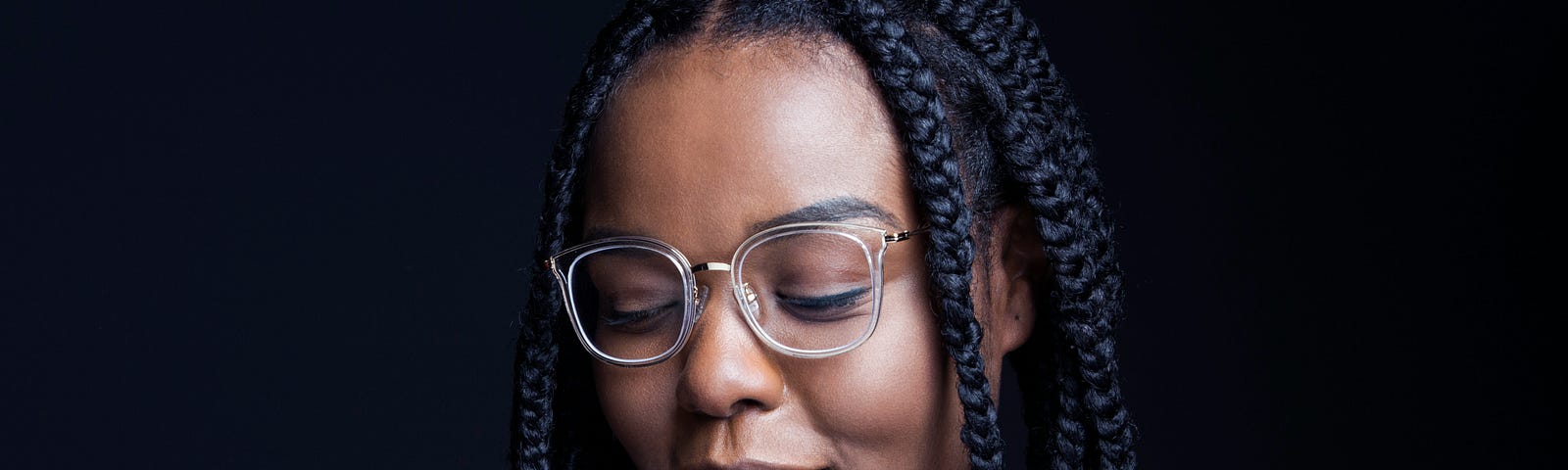 Black woman with braided hair wearing glasses and looking down.