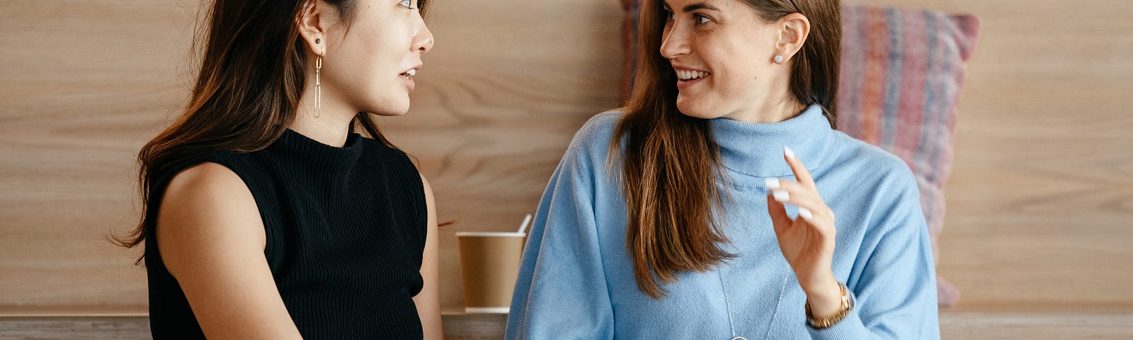 Two women talking to each other about work with a laptop in front of wooden stadium seating