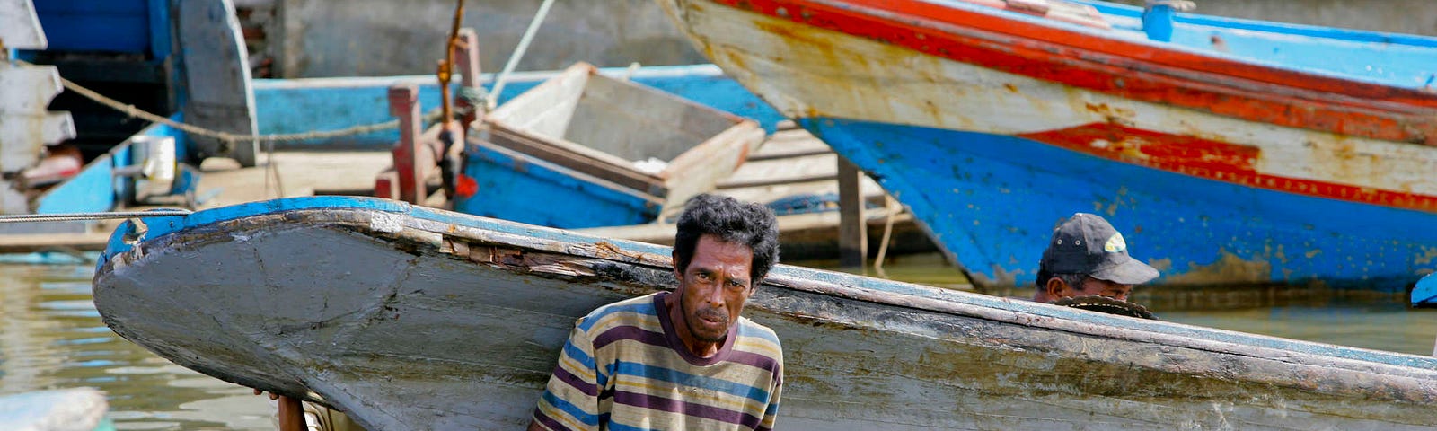 A man pulls a colourful fishing boat as he wades through the sea.