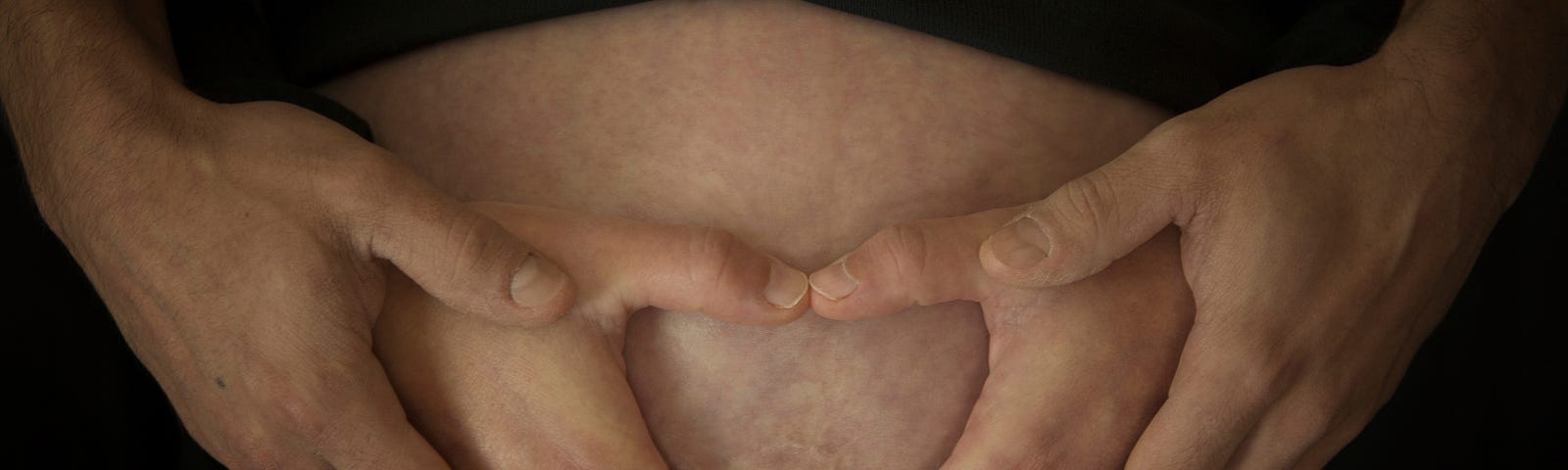 Multiple hands form the shape of a heart over a pregnant belly