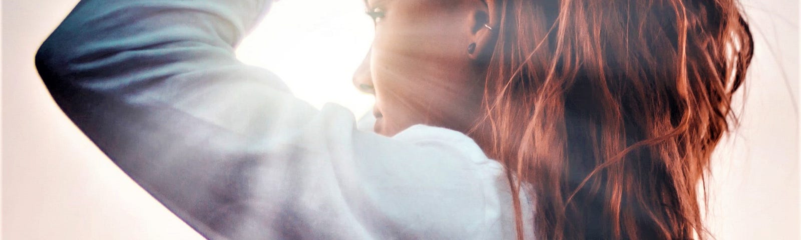 side view of girl with long red hair wearing long-sleeve top looking into sunny sky