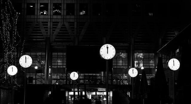 Black and white photo of several outdoor analog clock faces displaying midnight.