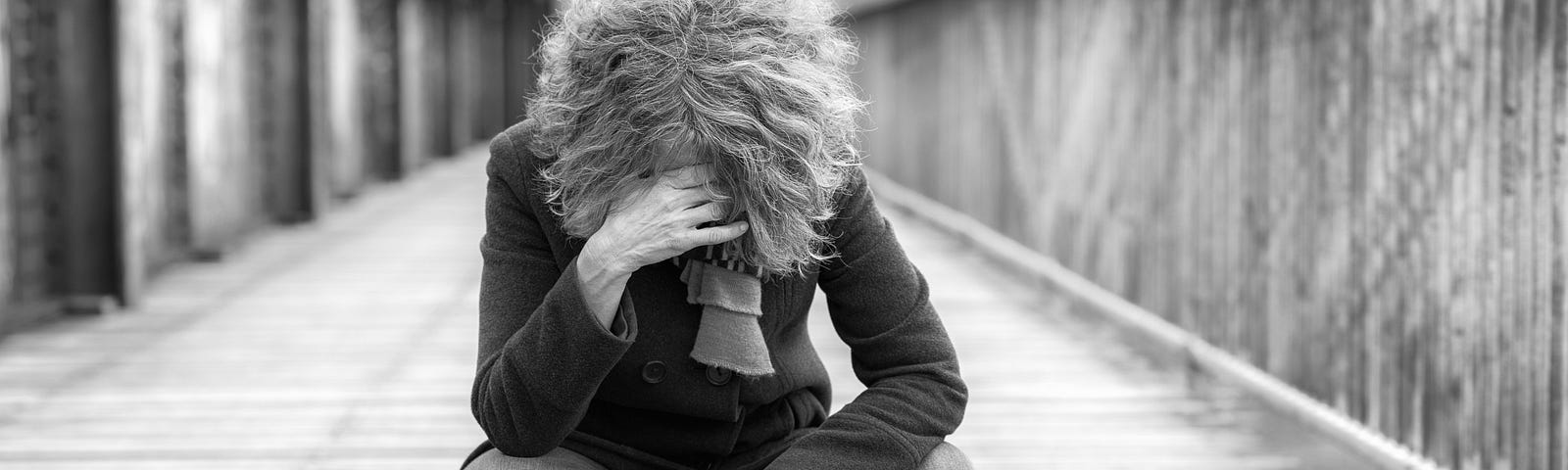 Dejected woman squatting on a bridge hanging her head with hand to her forehead outdoors on a cold day.