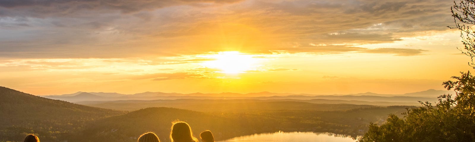 Group of women sits on the top of the mountain looking at sunset