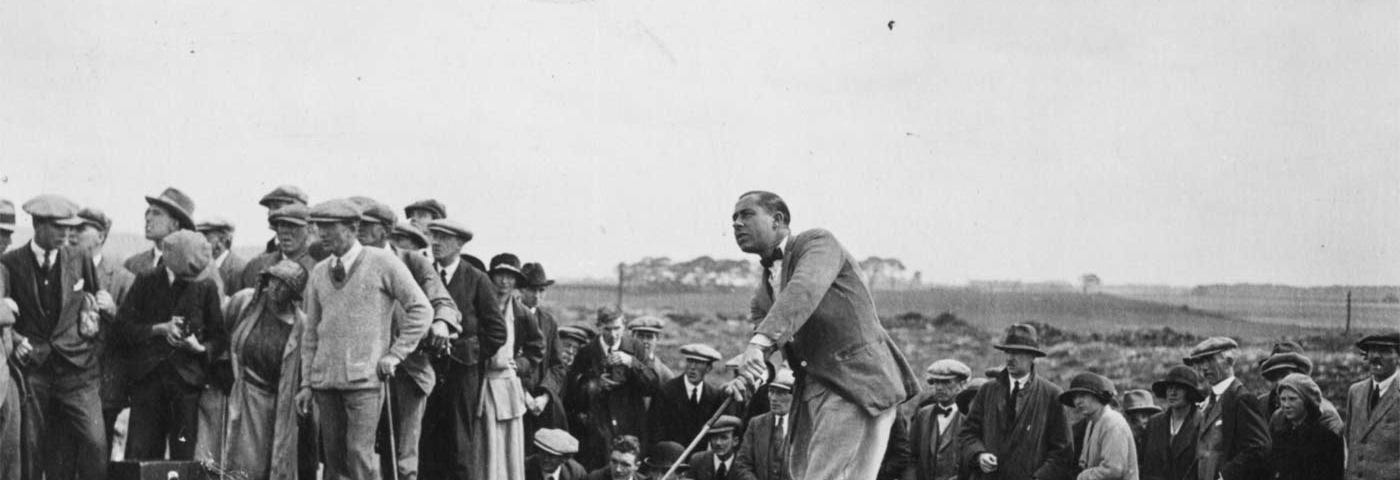 A black and white photo of Walter Hagen teeing off in 1922. A crowd of spectators surround him.