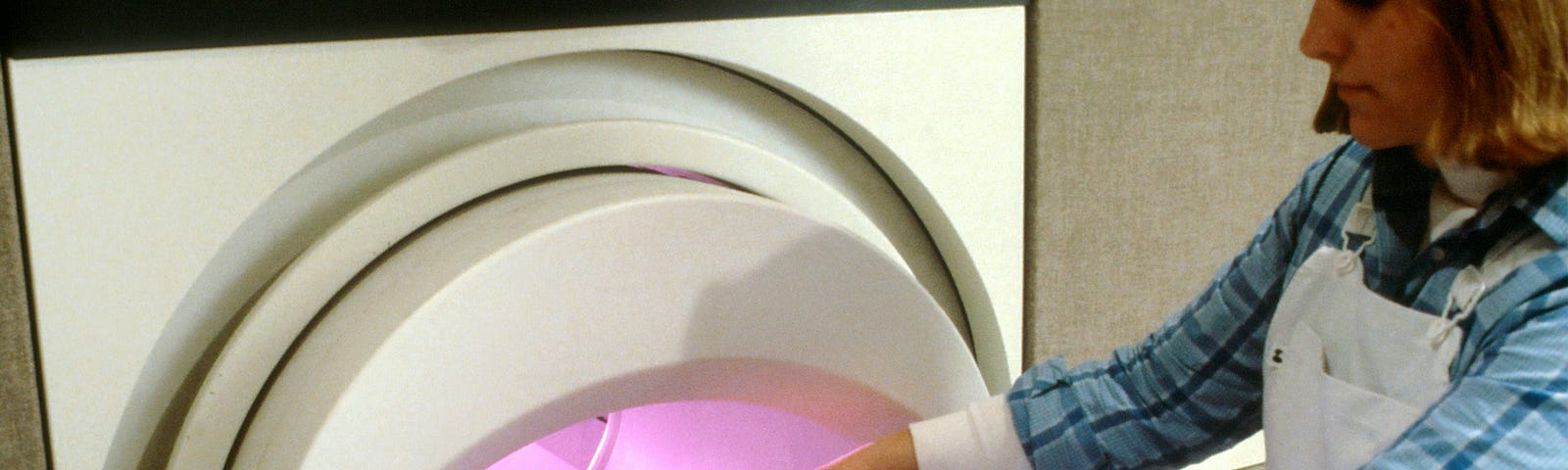 A woman is situated on an old MRI machine by a nurse.