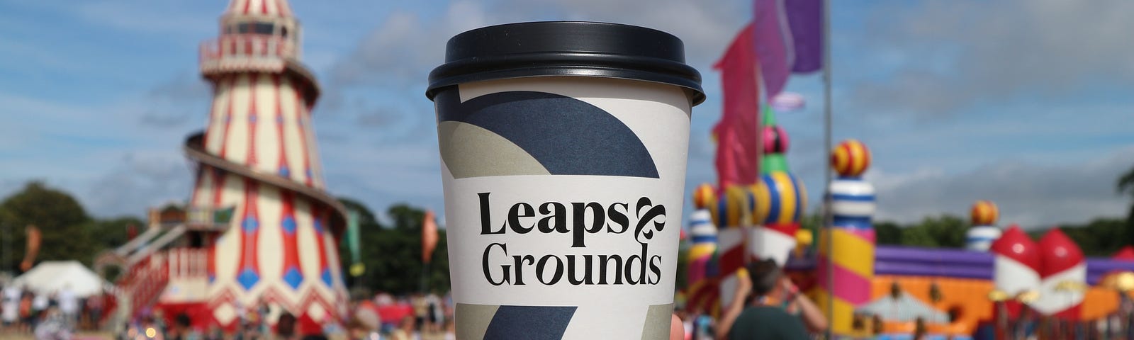 A Leaps & Grounds coffee cup in front of a blurry background showing a festival