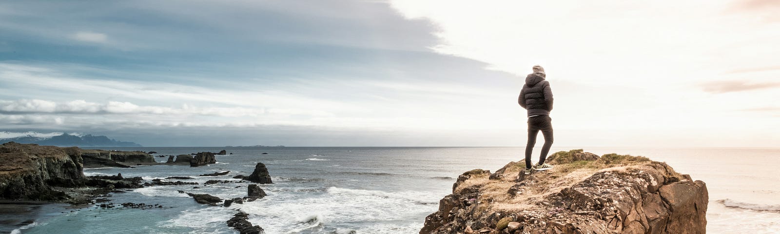 Man stands on a cliff overlooking ocean waters.