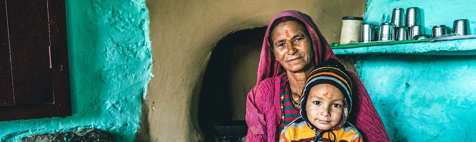 A child in the lap of a woman, probably grandmother, who is sits on the floor