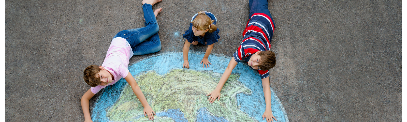 Three children lying on pavement with a large chalk drawing of the Earth, each with one hand touching the map, symbolizing their connection to and care for the planet. Brightly colored chalks are scattered nearby, adding a playful and creative touch to the scene