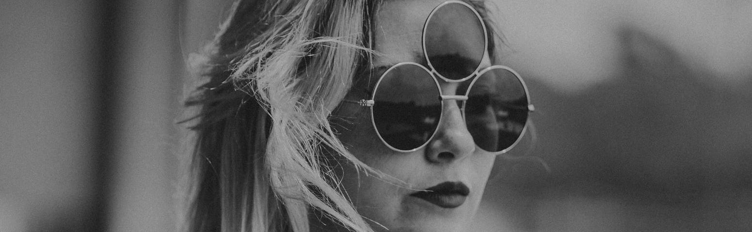 Grayscale photograph of a woman wearing sunglasses with three lenses, evoking the story title’s claim to weirdness.