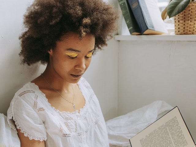 A woman wearing a white blouse reading a book.