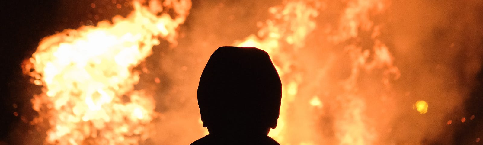 The silhouette of a man staring at a blazing fire.