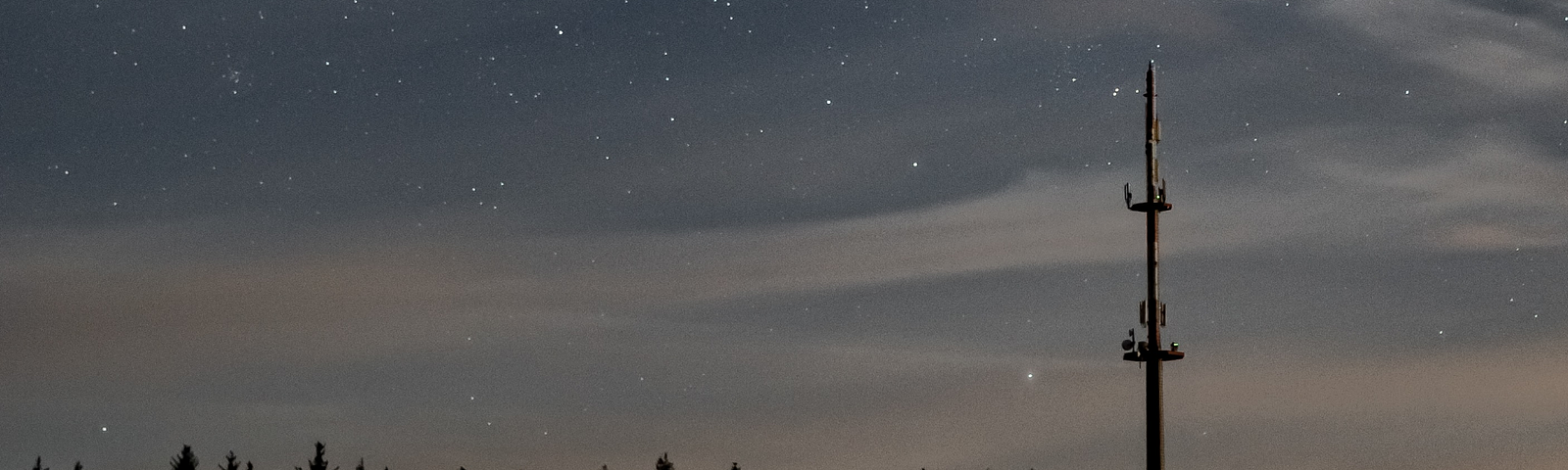 A radio tower alone in the woods at night.