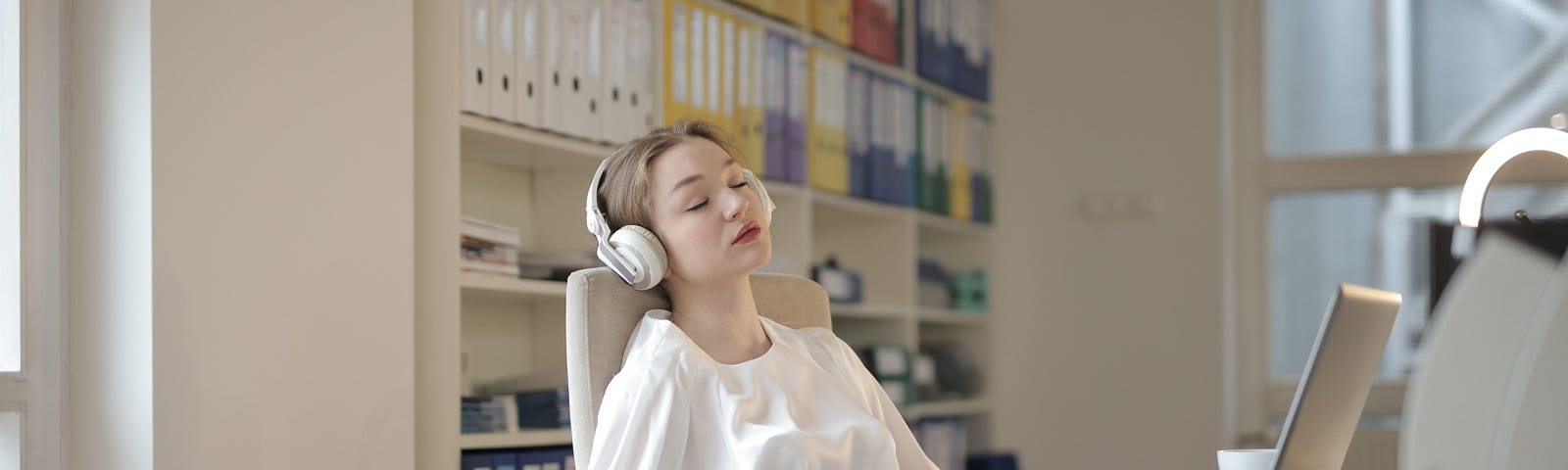 woman with headphones on snoozes in front of her desk.