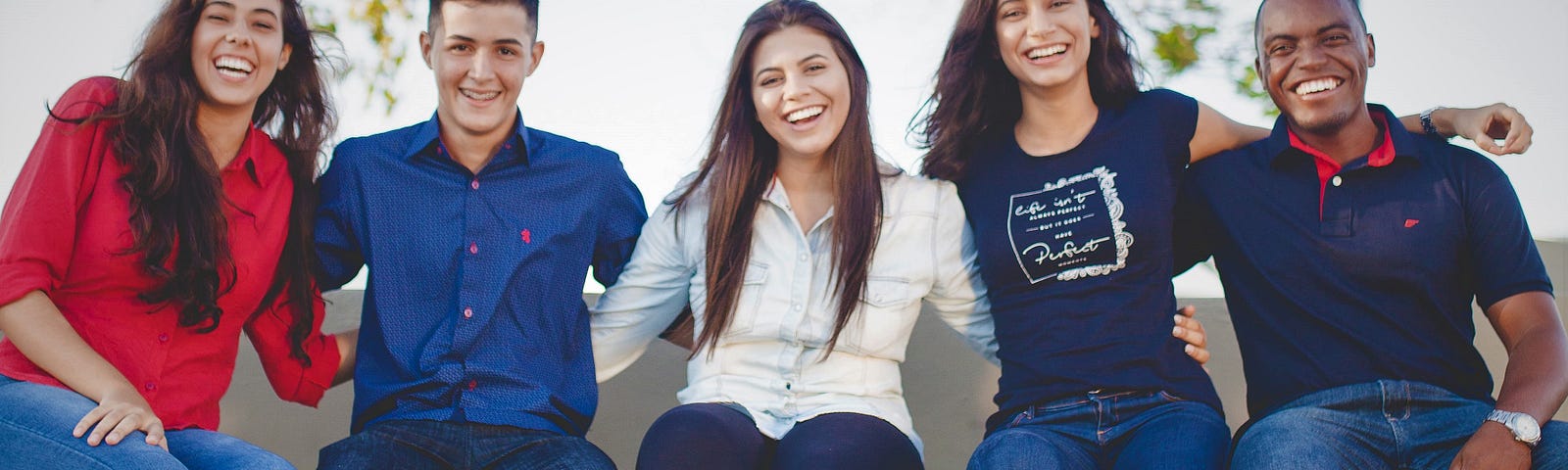 group of smiling friends sitting on wall