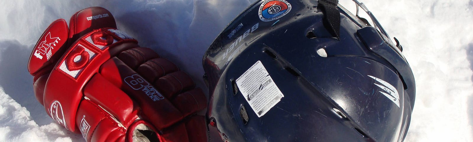 Hockey gloves and a helmet placed in a pile of snow.