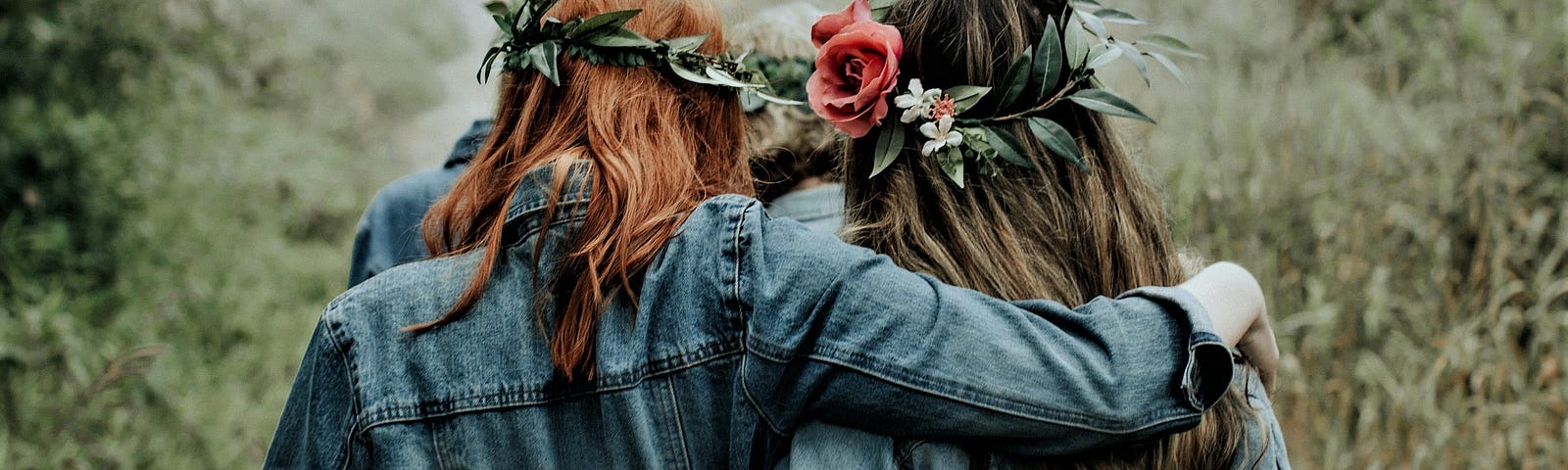 back view of two girls wearing denim jackets and flowers in their hair with arms around each other