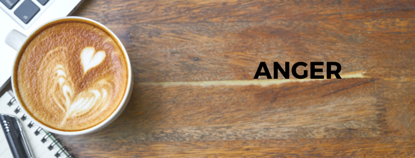 Coffee on a desk with heart-shaped foam next to the word Anger.