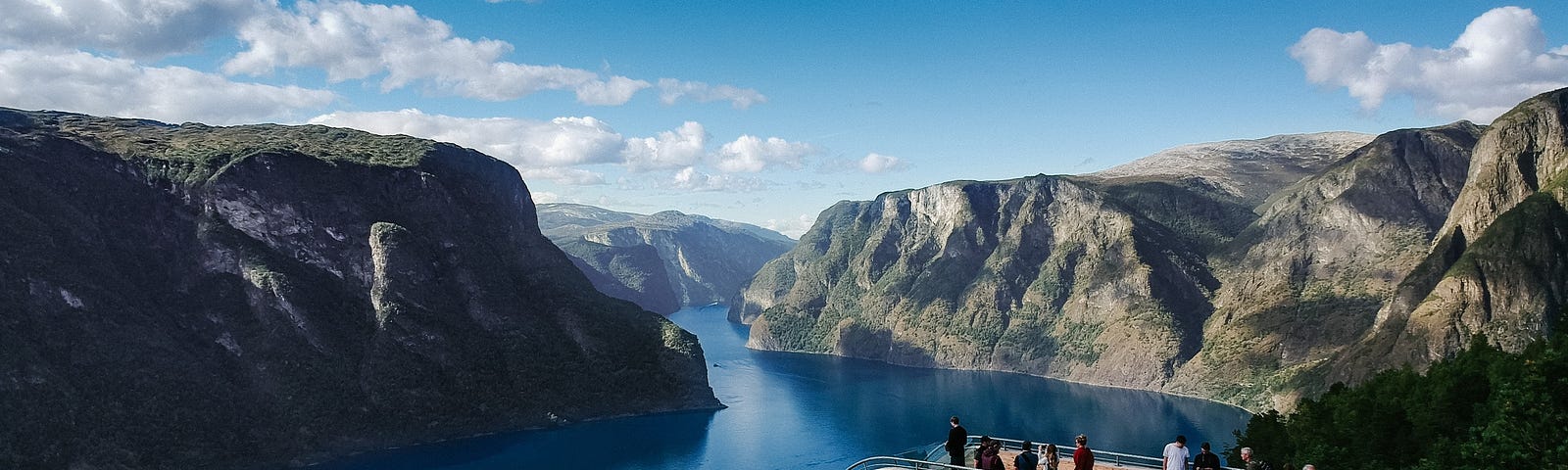 Beautiful view of hills with river winding through and bridge with people on it in foreground, but bridge curves to dip straight down.