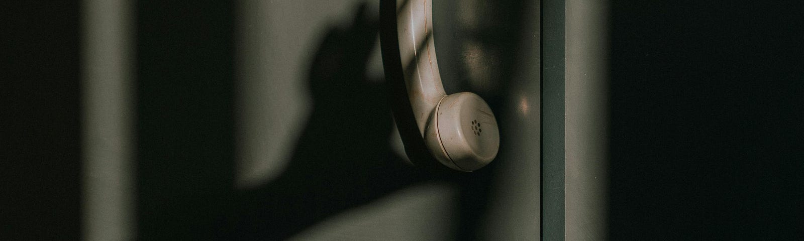 Tan phone receiver dangling with a shadow of a hand reaching for it.