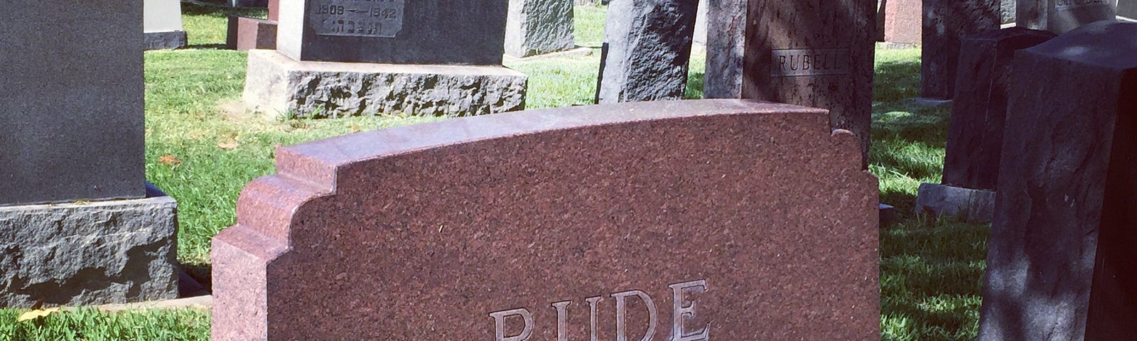 A graveyard with multiple headstones. In the center is a big red stone saying “ Rude” Due to Queen of England being put to rest on a Monday.